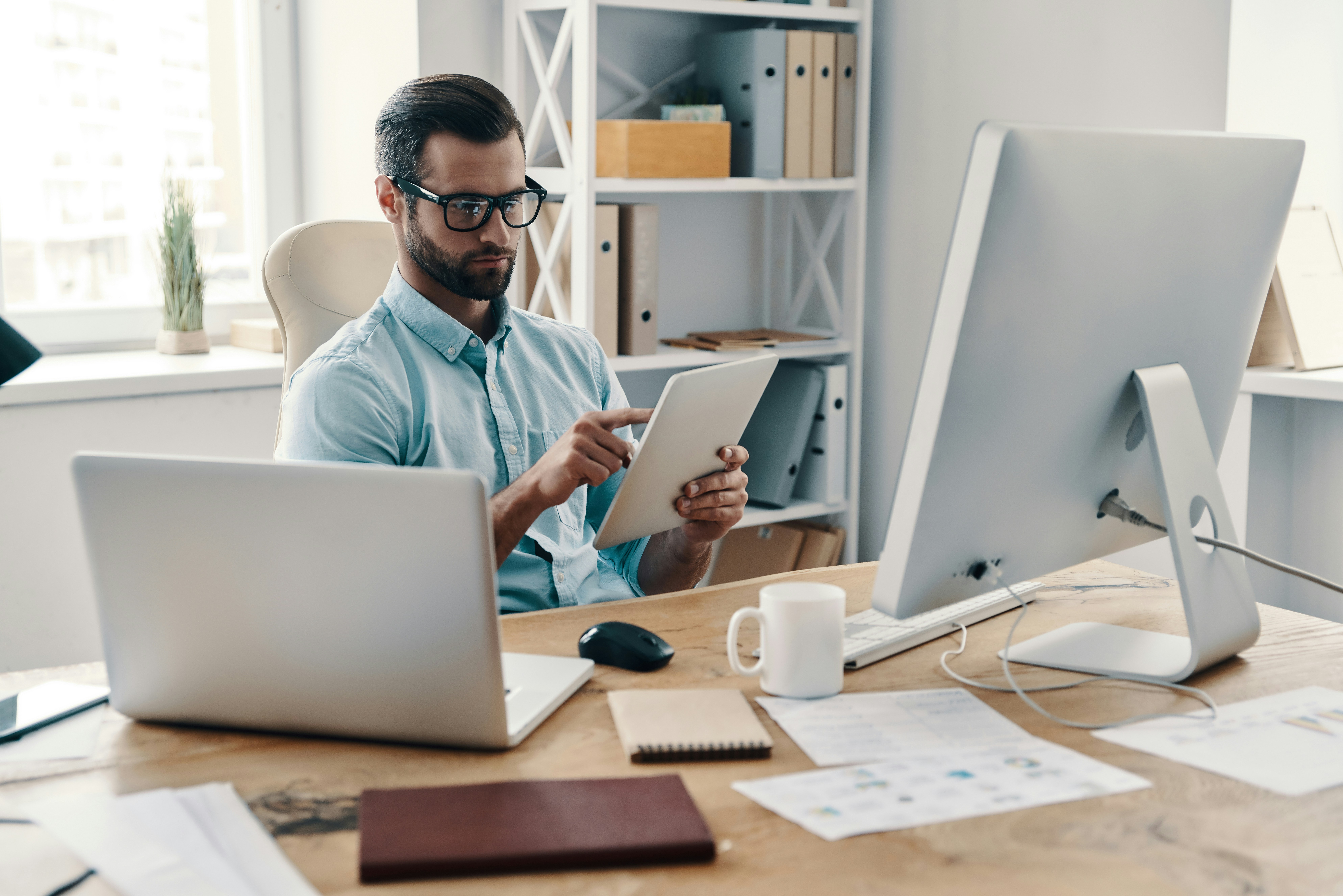 Conseiller clientèle particuliers préparant un rendez-vous client sur tablette et ordinateur dans une agence bancaire moderne